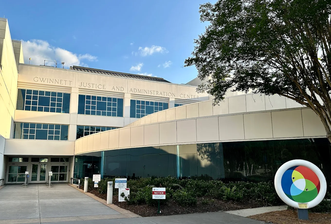 Exterior view of the Gwinnett Justice and Administration Center with a large tree and circular sculpture in front.